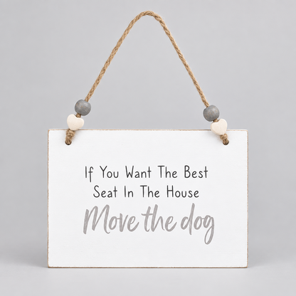 A white rectangular hanging wall sign with the phrase 'If You Want The Best Seat In The House Move the dog' in black and light gray lettering, suspended by a natural jute rope with small gray and cream wooden beads, on a plain white background.